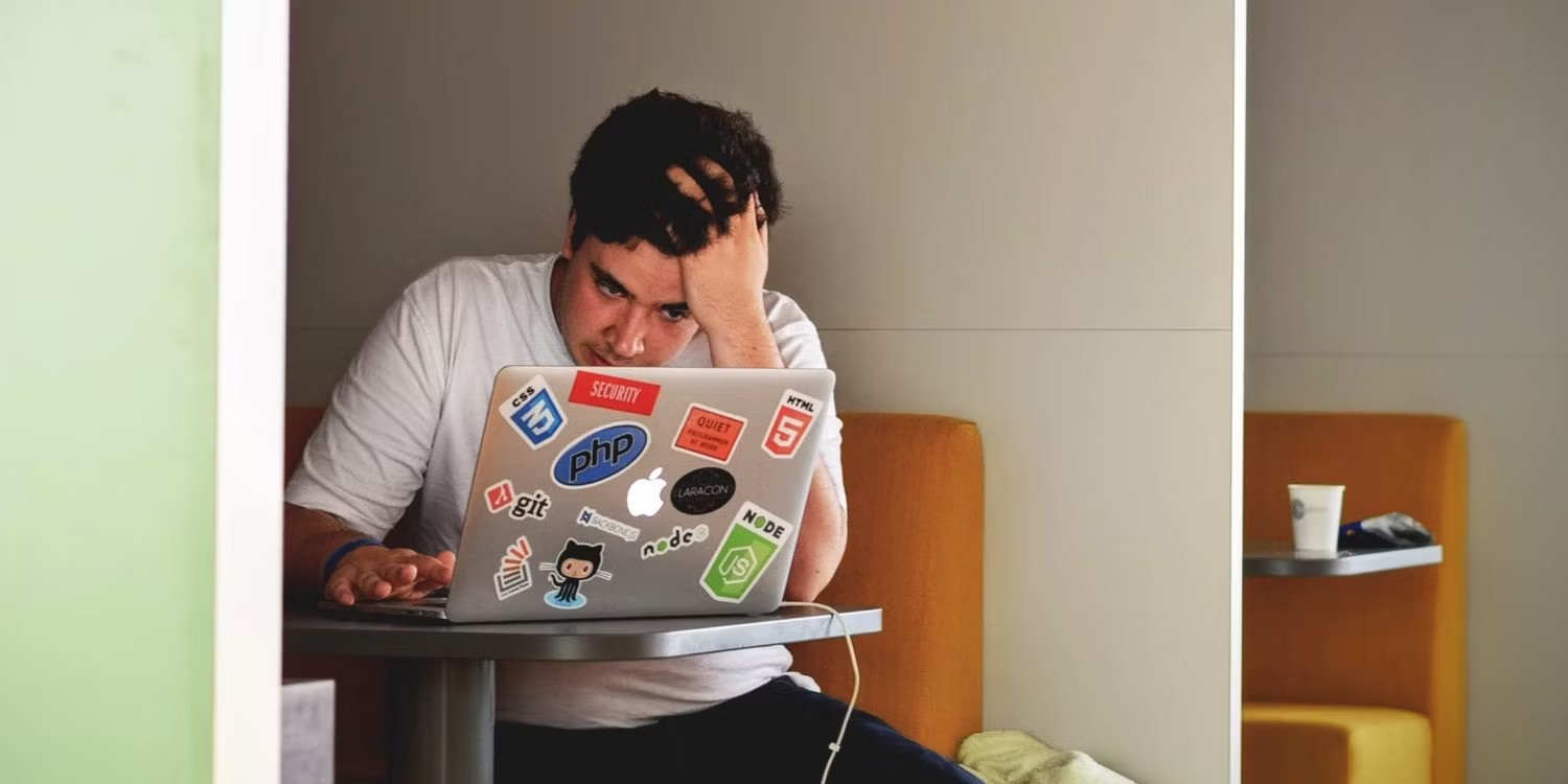 Man sitting infront of a MacBook with one of his hands on his forehead