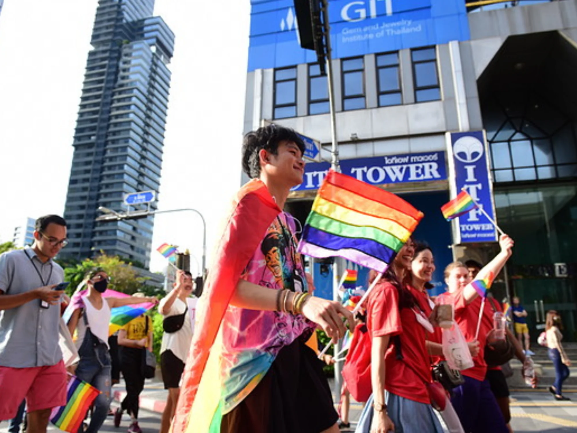 a colorful lgbtq protest taking place in thailand many people are gathered wearing colorful clothes and waving flags
