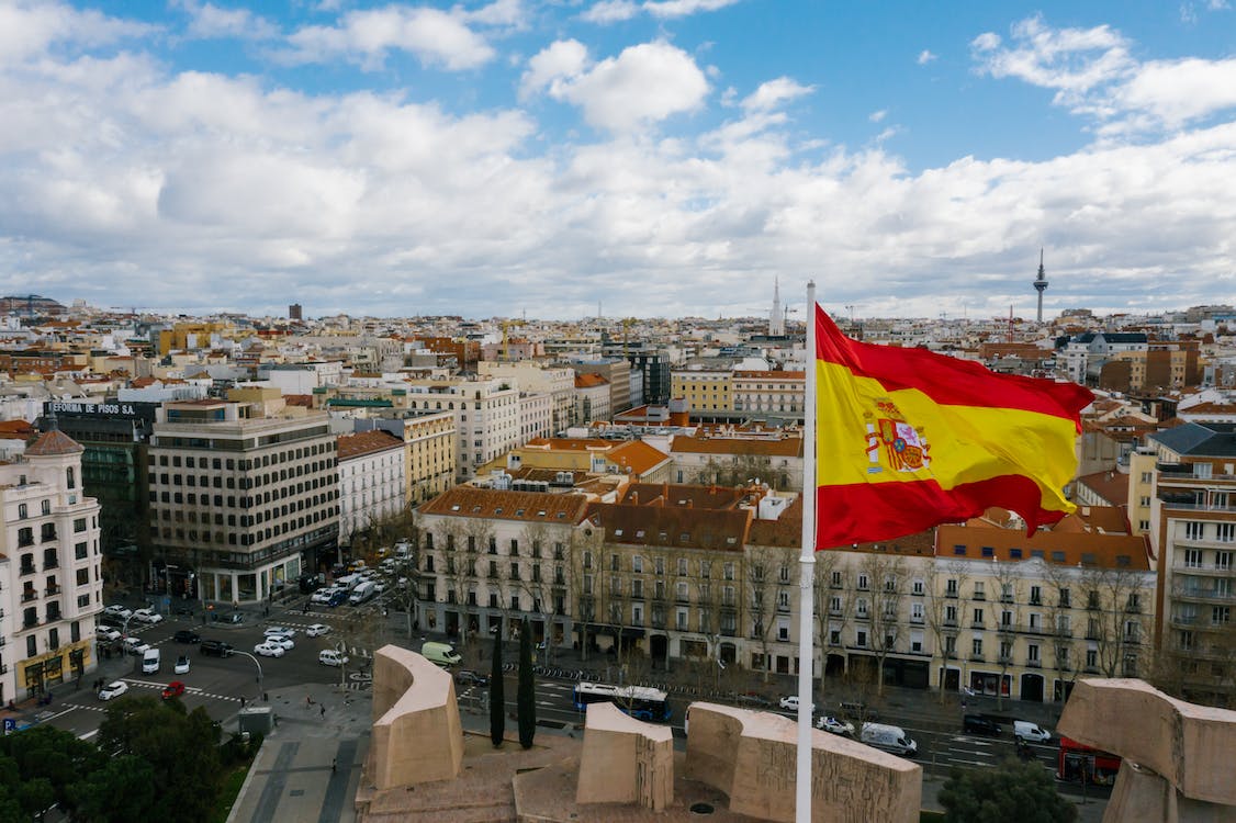 Free Drone view of Spanish city with aged buildings and national flag under cloudy blue sky Stock Photo