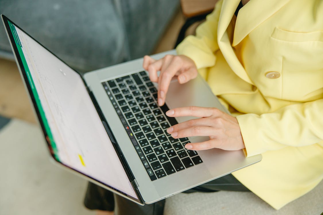 Free A Woman in a Yellow Jacket Typing on a Laptop Stock Photo